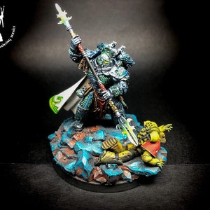 Puede incluir: Una miniatura de Space Marine verde y plateada con una lanza, de pie sobre una miniatura de Space Marine amarilla y roja caída. Las miniaturas están sobre una base rocosa con acentos azules y marrones.