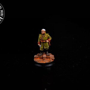 Może przedstawiać: Miniaturowa figurka oficera wojskowego w zielonym mundurze ze złotymi akcentami, czerwonymi mankietami i czarnymi butami. Figurka stoi na teksturowanej, okrągłej podstawie. Obraz zawiera tekst "YOUR NEXT COOL MINI".