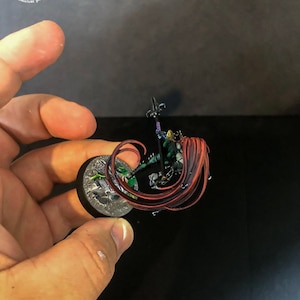 以下が含まれることがあります： 緑色の鎧を着て槍を持った、長い赤い髪の女性戦士のミニチュアフィギュア。フィギュアは複雑なディテールでペイントされており、丸い台座の上に立っています。