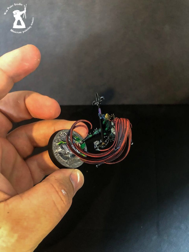 以下が含まれることがあります： 緑色の鎧を着て槍を持った、長い赤い髪の女性戦士のミニチュアフィギュア。フィギュアは複雑なディテールでペイントされており、丸い台座の上に立っています。