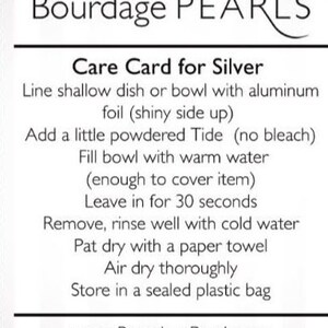 Pu&ograve; includere: Una scheda di cura rettangolare bianca per gioielli in argento di Bourdage PEARLS. Il testo fornisce istruzioni: rivestire un piatto con carta stagnola, aggiungere detersivo Tide in polvere, riempire con acqua tiepida, immergere per 30 secondi, risciacquare, asciugare e conservare. Sito: www.BourdagePearls.com.