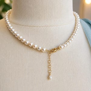Pu&ograve; includere: Una collana composta da un singolo filo di perle rotonde color crema. La collana include una chiusura a moschettone in metallo dorato e una catenella di estensione regolabile che pende, terminata da una piccola perla singola all'estremit&agrave;.