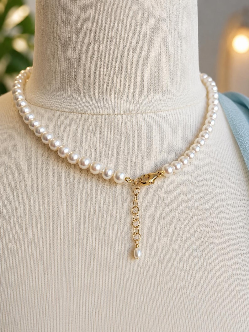Pu&ograve; includere: Una collana composta da un singolo filo di perle rotonde color crema. La collana include una chiusura a moschettone in metallo dorato e una catenella di estensione regolabile che pende, terminata da una piccola perla singola all'estremit&agrave;.