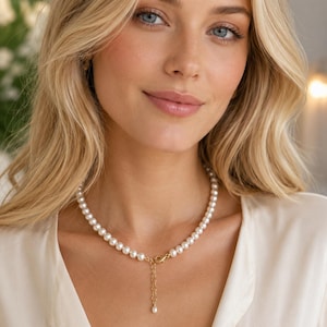Pu&ograve; includere: Una collana composta da un filo di perle bianche rotonde con una chiusura a moschettone in metallo color oro. Una corta catenella di estensione dorata pende dalla chiusura, terminando con una singola piccola perla all'estremit&agrave;.