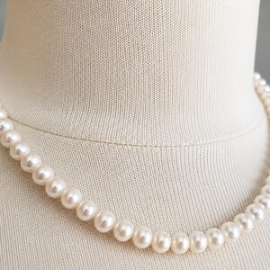 Pu&ograve; includere: Una collana a filo singolo composta da perle rotonde e uniformi di colore bianco sporco. Le perle presentano una superficie liscia e lucente, infilate in una linea continua che poggia su un busto espositore in tessuto di colore neutro.