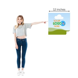 May include: A poster with a blue sky, green hills, and a white cloud. The poster is 30.48 cm wide and features the text "YOUR LOGO HERE" with a logo. A person is pointing at the poster.