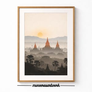 Könnte beinhalten: Gerahmter Kunstdruck mit einer ruhigen Landschaft mit alten Tempeln bei Sonnenaufgang. Das Kunstwerk zeigt eine warme Farbpalette mit Orange- und Brauntönen und eine goldene Sonne. Die Tempel sind vor dem nebligen Hintergrund silhouettiert.