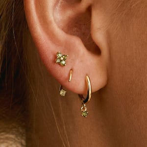 May include: A set of three ceramic mugs with a speckled, matte finish. The mugs are in shades of cream, light brown, and dark brown. Each mug has a simple, minimalist design and a rounded handle.