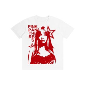 Puede incluir: Camiseta blanca con un gráfico rojo de una mujer y el texto "PINK PANTHERESS" en rojo. Dos estrellas rojas también están en el diseño. La camiseta es de cuello redondo.