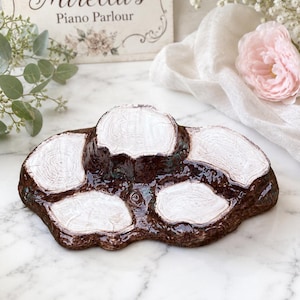 May include: A ceramic display stand featuring a dark brown, glossy bark-like texture with five raised, flat, white-painted circular surfaces that resemble cross-sections of tree stumps, arranged in an irregular, organic cluster shape.