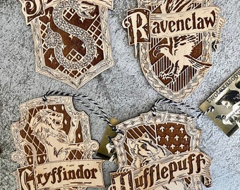 May include: Four wooden ornaments featuring the Hogwarts house crests: Gryffindor, Hufflepuff, Slytherin, and Ravenclaw. Each crest is intricately carved with the house mascot and name.