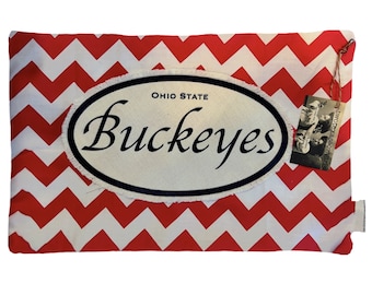 May include: Red and white chevron patterned pillow with a white oval patch that says "Ohio State Buckeyes" in black lettering.