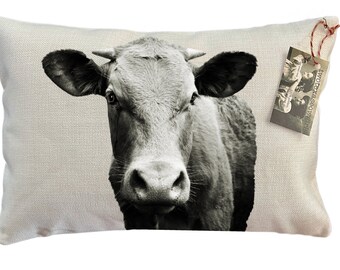 May include: A black and white photograph of a cow's face printed on a beige pillow with a small tag that says "Two Texas Cowgirls".