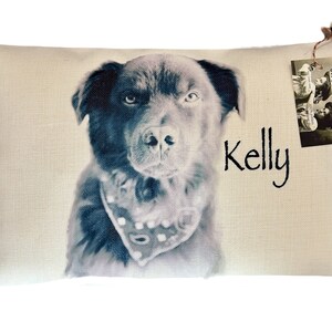 May include: A beige pillow with a black and white photo of a dog wearing a bandana. The dog's name, "Kelly", is written in black text below the photo.