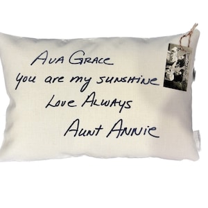 May include: A white pillow with black handwritten text that reads "Ava Grace you are my sunshine Love Always Aunt Annie". A small black and white photo is attached to the pillow with a string.