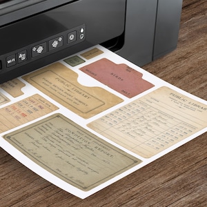 May include: A sheet of printed paper emerging from a black printer featuring vintage-style library ephemera. The designs include a Public Library book pocket, a condition report form, and various checkout cards with text like Birds and Public Library.