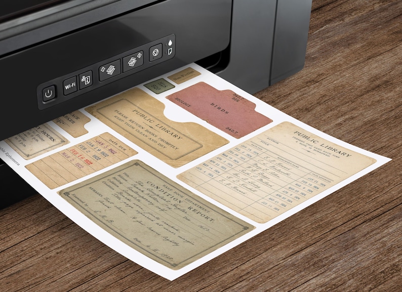 May include: A sheet of printed paper emerging from a black printer featuring vintage-style library ephemera. The designs include a Public Library book pocket, a condition report form, and various checkout cards with text like Birds and Public Library.