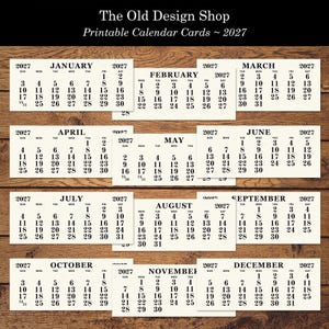 May include: Printable calendar cards for 2027, featuring each month with dates and days of the week. The Old Design Shop logo is at the top. The calendars are arranged on a wooden surface.