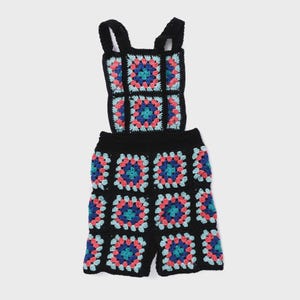 May include: Black crochet romper with colorful square patterns. The squares feature pink, blue, and teal designs. The romper has a bib top with straps and shorts. The garment is handmade and has a unique, bohemian style.