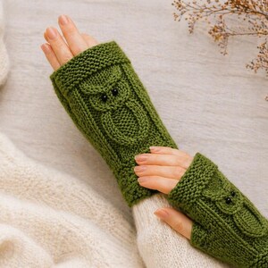 May include: A pair of green knitted fingerless gloves with an owl design. The gloves are a vibrant green color and feature a detailed owl face on the back of the hand. The owl's eyes are small, dark beads.