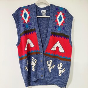 Könnte beinhalten: Eine blaue Strickweste mit V-Ausschnitt und Knopfleiste. Das Kleidungsstück zeigt ein farbenfrohes Muster mit roten, weißen und türkisfarbenen geometrischen Formen, darunter Rautenmotive und Kaktusdesigns. Ein Napa Valley Etikett ist sichtbar.