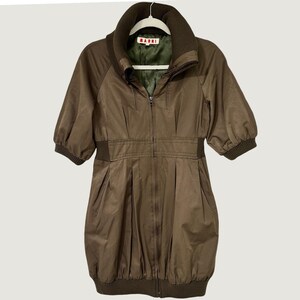 May include: A brown zip-up jacket with a high ribbed collar, half-length sleeves with ribbed cuffs, and a ribbed hem. The jacket features a full-length front zipper, a gathered waistline, and an olive green interior lining with a Marni brand label.