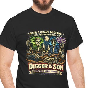 May include: Black t-shirt featuring a graphic with the text "AVOID A GRAVE MISTAKE - CALL THE PROFESSIONALS" and "DIGGER & SON CREMATION & BURIAL SERVICES". The graphic depicts skeletons with shovels. The shirt is worn by a person.