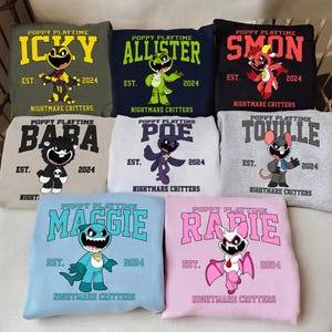 Könnte beinhalten: Eine Auswahl an Sweatshirts mit Charakteren aus "Poppy Playtime". Jedes Sweatshirt zeigt den Namen eines Charakters, das Jahr "2024" und den Schriftzug "Nightmare Critters". Die Sweatshirts sind in verschiedenen Farben erhältlich, darunter Grün, Marineblau, Schwarz, Grau und Rosa.