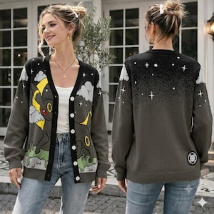 May include: A charcoal gray button-down cardigan featuring a graphic of a black creature with yellow accents, a crescent moon, and clouds on the front. The back displays a starry night sky pattern with a small circular patch near the hem.