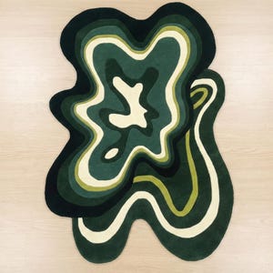 Könnte beinhalten: Ein abstrakter Teppich in Grün-, Creme- und Schwarztönen mit einem geschichteten, fließenden Design. Die organische Form des Teppichs erzeugt einen modernen, künstlerischen Look. Das Design ähnelt einer topografischen Karte. Geeignet für Wohn- oder Schlafzimmer.