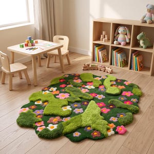 May include: An irregular, tufted area rug featuring a deep green base with raised, textured patches of light green moss-like shapes and a variety of colorful, multi-petaled flowers in shades of pink, purple, orange, and white scattered throughout.