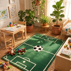 May include: A green rectangular rug with a soccer field design, featuring a black and white soccer ball in the center. The rug is surrounded by a wooden table and chairs, toys, and potted plants, creating a playful and inviting space.