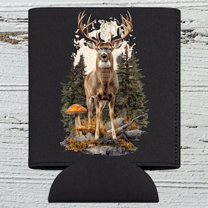 May include: Black can cooler featuring a majestic buck with large antlers, set against a backdrop of a forest and a full moon. The design includes pine trees, mushrooms, and a rocky ground, creating a nature-themed aesthetic.