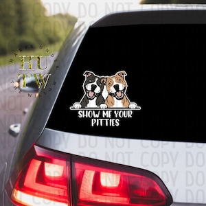 May include: A black and white car window sticker with two cartoon pit bull dogs peeking over a white banner with the text "Show Me Your Pitties".