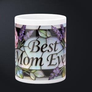 May include: White ceramic mug with a stained glass design. The mug features the text "Best Mom Ever" in a decorative font, surrounded by lavender and pink flowers. The mug has a black background.