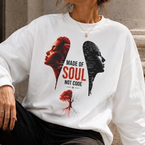 May include: A white long-sleeve sweatshirt featuring a graphic print of two side profiles facing away from each other, one in red and one in black, with the text "MADE OF SOUL NOT CODE" and a small tree graphic split in red and black colors.