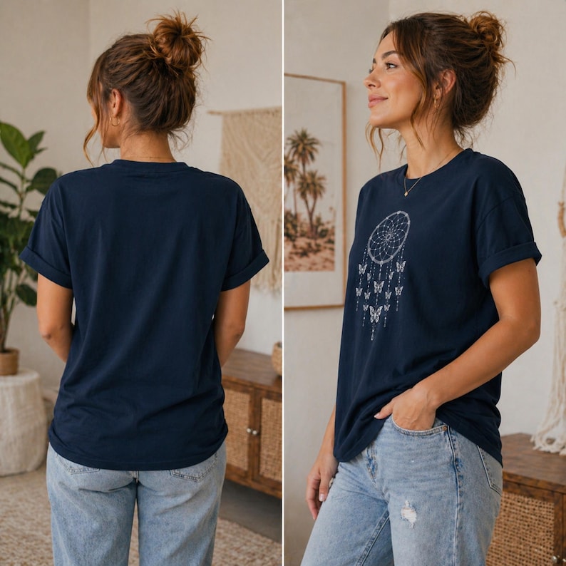 May include: A navy blue short-sleeve t-shirt featuring a white graphic print of a dreamcatcher with hanging butterflies on the front. The shirt has a crew neckline and rolled sleeves, paired with light blue denim jeans shown from two angles.