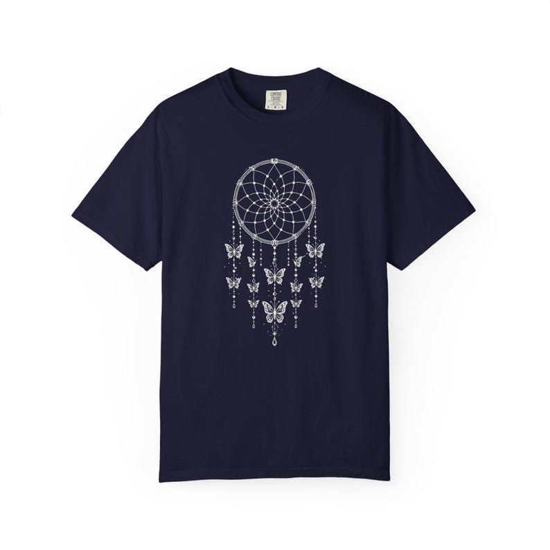 May include: A dark navy blue short-sleeve t-shirt featuring a white graphic print of a dreamcatcher centred on the chest. The dreamcatcher design includes intricate web detailing, hanging beaded strings, and several butterfly silhouettes.