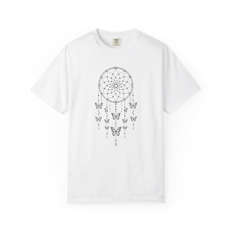 May include: A white short-sleeved t-shirt featuring a black line art graphic on the chest. The design depicts a circular dreamcatcher web with multiple dangling strings adorned with small beads and several butterflies of varying sizes.
