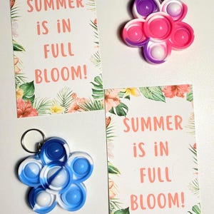 May include: Two flower-shaped keychains in pink, purple, and blue, with white accents. Two cards with floral borders and the text "SUMMER IS IN FULL BLOOM!" are also present. The keychains are a fun, colorful accessory.