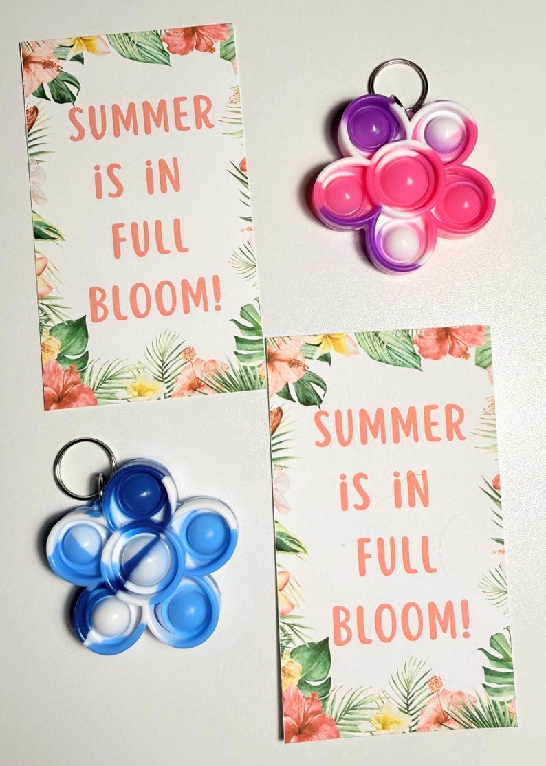 May include: Two flower-shaped keychains in pink, purple, and blue, with white accents. Two cards with floral borders and the text "SUMMER IS IN FULL BLOOM!" are also present. The keychains are a fun, colorful accessory.