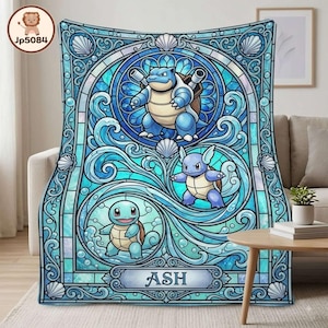 May include: A rectangular fleece blanket featuring a blue stained-glass style design with three water-type creatures. The blanket displays Blastoise, Wartortle, and Squirtle surrounded by swirling water patterns, seashells, and the name ASH.
