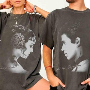 May include: Two charcoal gray t-shirts featuring black and white portraits. One shirt displays a side profile of a woman with the text "Padme Amidala." The other shirt shows a man's profile with the text "Anakin Skywalker."
