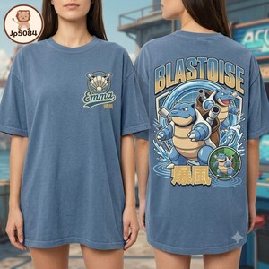 May include: A blue t-shirt featuring a small graphic on the front chest with a shell icon and the name Emma. The back displays a large graphic of the character Blastoise with water effects, the text BLASTOISE, and Japanese characters.