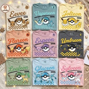 May include: A collection of nine t-shirts in various colors, each featuring a different Pokemon character, the name of the character, the year 1996, a Poke Ball graphic, and a checkered pattern at the bottom. The shirts are arranged in a grid.