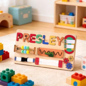 May include: Wooden activity board with the name "PRESLEY" spelled out in colorful letters. Features include an abacus, zipper, buckle, and gears. A green alligator is also present. Designed for early childhood development.