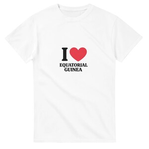 Puede incluir: Camiseta blanca con el texto "I ♥ EQUATORIAL GUINEA". La "I" es negra, el corazón es rojo y el texto es negro. Una camiseta informal.
