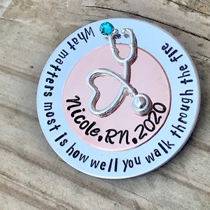 May include: A silver and rose gold round charm with a stethoscope and heart design. The charm has the text "What matters most is how well you walk through all the" and "Nicole, RN, 2020".