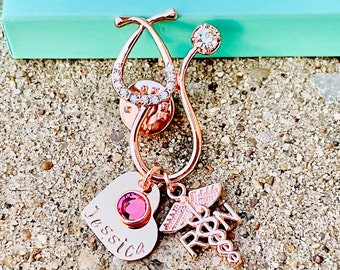 Könnte beinhalten: Rosenfarbener Stethoskop-Anhänger mit einem rosa Kristall-Herz-Anhänger, einem medizinischen Symbol-Anhänger und einem personalisierten Namensschild mit der Aufschrift "Jessica".