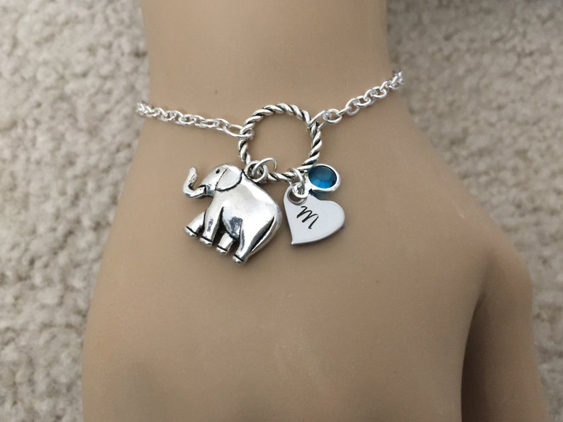 Puede incluir: Pulsera de plata con un dije de elefante, un dije de coraz&oacute;n con la letra "M" grabada y una piedra preciosa azul.